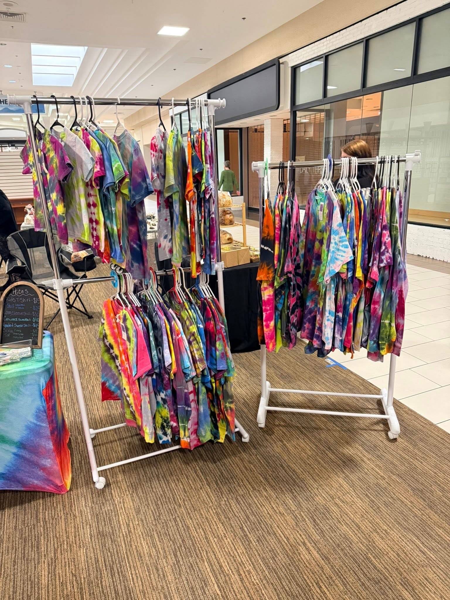 Racks of colorful AlliPop tie-dye shirts at a market