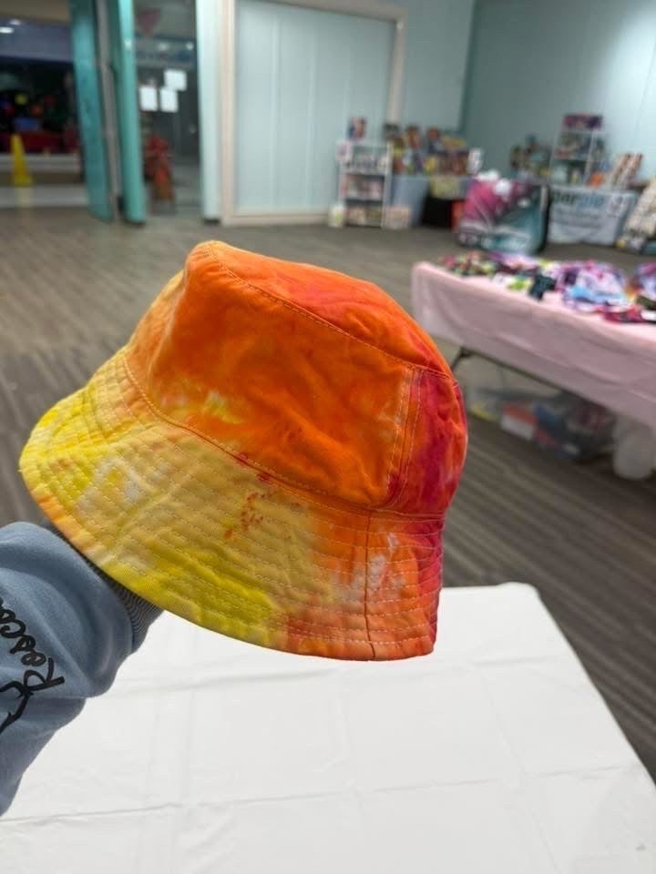 Orange, yellow and red tie-dye bucket hat held up at a market